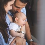 Parents holding their young baby boy, him sleeping.