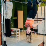 Adult woman doing an upside-down pose on a reformer pilates machine in a fitness studio.