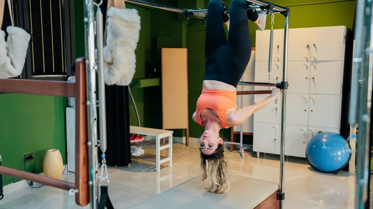 Adult woman doing an upside-down pose on a reformer pilates machine in a fitness studio.